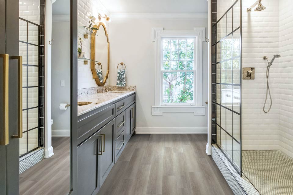 wood look vinyl flooring in bathroom with large tiled shower and grey cabinets and mixed metal decor.